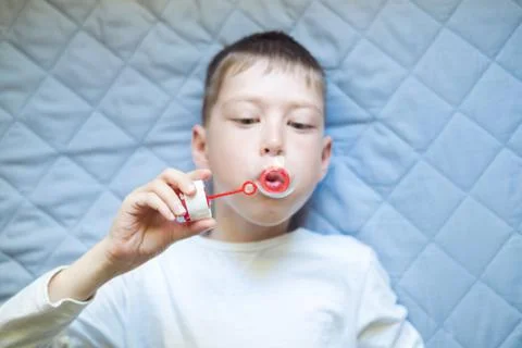 Boy lying on the bed blowing soap bubbles, close-up. portrait of a child with Stock Photos
