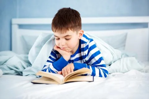 Boy lying in bed with a book Stock Photos