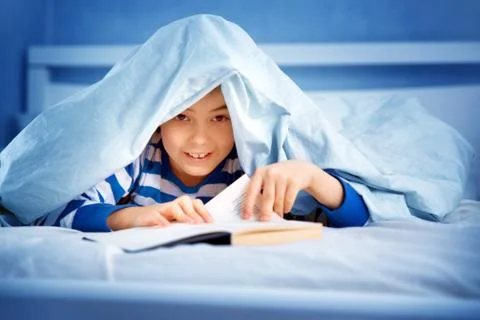 Boy lying in bed with a book Stock Photos