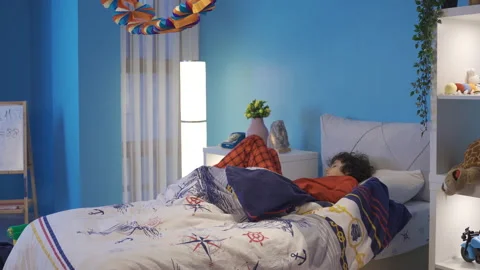 Boy lying in bed at night wakes up and looks out the window. To hear, to be afra Video stock 227678554
