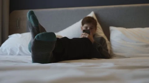 The boy is lying on the bed with a smartphone in his hands. Communication and 動画素材 99003829