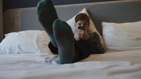 The boy is lying on the bed with a smartphone in his hands. Communication and 動画素材 99073237
