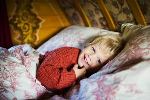 A boy lying in bed under a curved bow top roof of a gypsy caravan, looking at Stock Photos