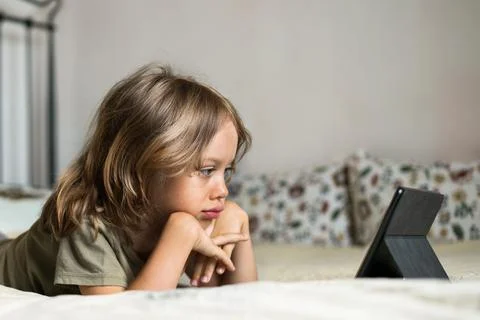 Boy lying on the bed using digital tablet computer playing games or watching Stock Photos