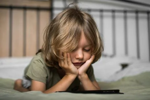 Boy lying on the bed using digital tablet computer playing games or watching Stock Photos