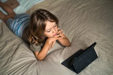 Boy lying on the bed using digital tablet computer playing games or watching Stock Photos