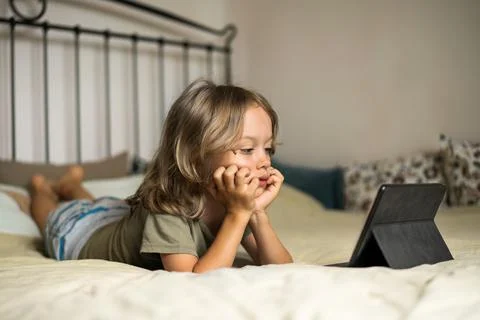 Boy lying on the bed using digital tablet computer playing games or watching Stock Photos