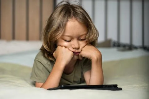 Boy lying on the bed using digital tablet computer playing games or watching Stock Photos
