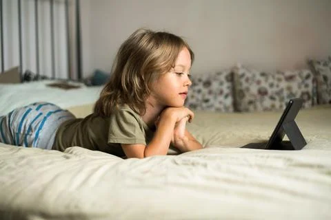 Boy lying on the bed using digital tablet computer playing games or watching Stock Photos