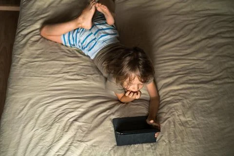 Boy lying on the bed using digital tablet computer playing games or watching Stock Photos