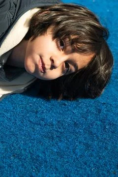Boy lying on blue carpet surface looking at camera Stock Photos