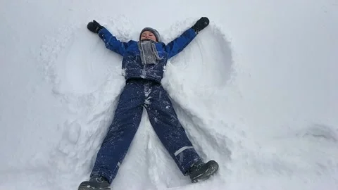 The boy is lying in a blue jacket in the snow. the image of an angel in the snow Stock Footage 149198192