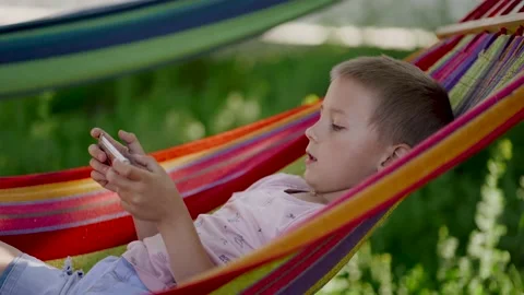 The boy is lying on a bright hammock and playing on the phone. Video stock 144382612