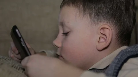The boy is lying on the couch and is playing on the tablet Stock Footage 73570628