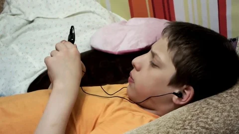 The boy is lying on the couch and is playing in the phone Stock Footage 74759192