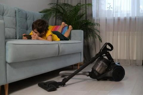 Boy is lying on the couch and playing on the phone, next to him on the floor is Stock Photos