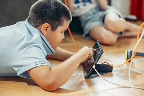 Boy lying on floor playing on tablet smartphone, near power outlet, charging Stock Photos