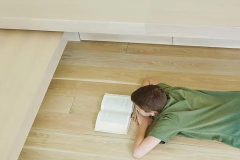 Boy lying on floor, reading book, high angle view Stock Photos
