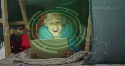 Boy lying in fort holding tablet, glow causing HUD and code appearing, engaging Stock Footage 331460959