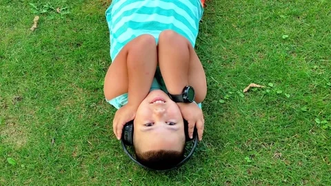 Boy Lying on Grass with Headphones Looking Around in Park Stock-Footage 342589339