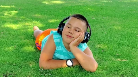 Boy Lying on Grass with Headphones Looking Around in Park Stock Footage 342589372