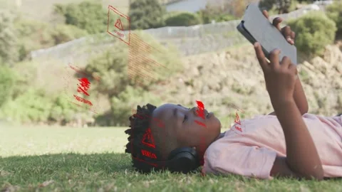 Boy lying on grass holding tablet, emitting malware warnings, tech icons Stock Footage 333648176