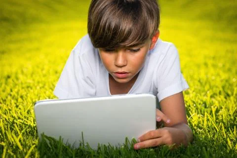 Boy lying on the grass reads the tablet Stock Photos