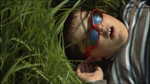 The boy is lying in the grass in the sun-glasses Stock Footage 75673161