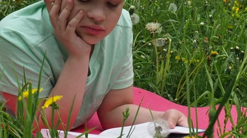 Boy  lying on green grass and reading book in park on summer clear day. Stock Footage 274167045