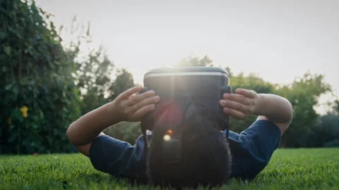 Boy lying on his back and wearing a virtual reality headset in a garden Stock Footage 275287954