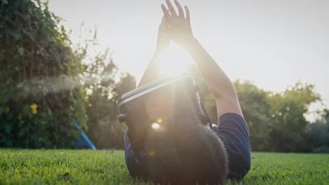 Boy lying on his back while looking into a virtual reality headset outdoors Stock Footage 275286131