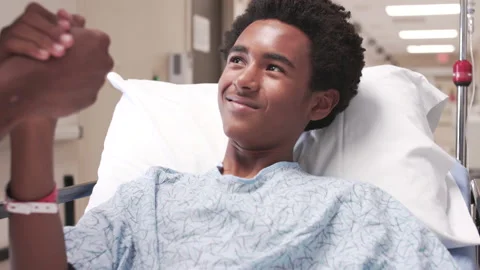 Boy lying in hospital bed and holding doctors hand Stock Footage 149040677
