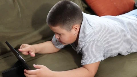 Boy lying on olive couch with digital tablet in blue striped shirt, indoor 動画素材 315429527