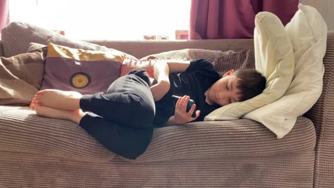 Boy lying on a settee watching videos on his mobile phone Stock Footage 177647714