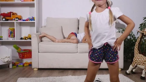 The boy is lying on the sofa, and the girl is running around the room Stock Footage