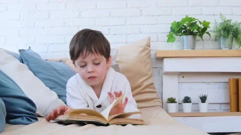 The boy is lying on the sofa and reading a book . Reading books. Development of Stock Footage 167039708
