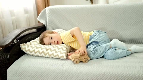 Boy is lying on sofa, is bored, playing with toy car. Video stock 196923295