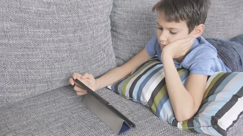 Boy lying on sofa with digital tablet computer at home. Technology, distance Stock Footage 129667908