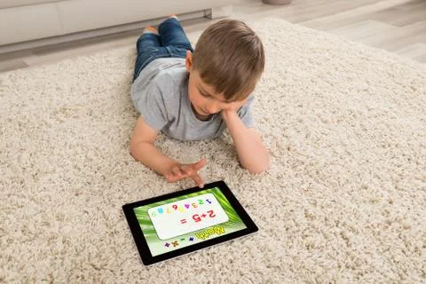 Boy Lying On Sofa Solving Math Problem On Digital Tablet At Home Stock Photos