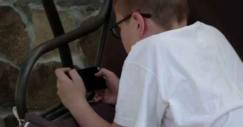 Boy Lying on the Swing Bench and Playing Game on Smartphone Stock Footage 64767537