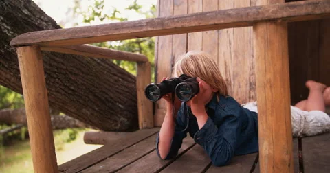 Boy lying in a treehouse looking through binoculars Stock Footage 61295879