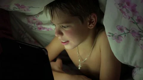 Boy lying under blanket and watching cartoons on touch pad Видео 68369643