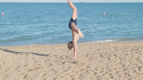 Boy makes an acrobatic element on sandy beach of sea 스톡 동영상 278989607