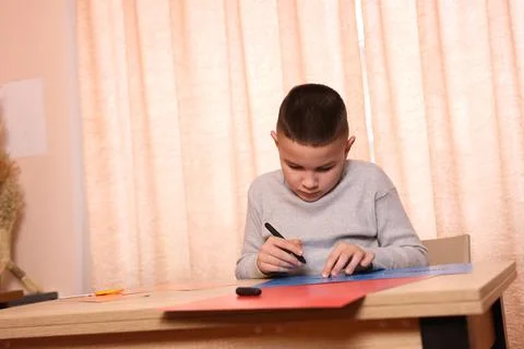 A boy makes applications from colored paper while sitting at a table. The con Foto stock
