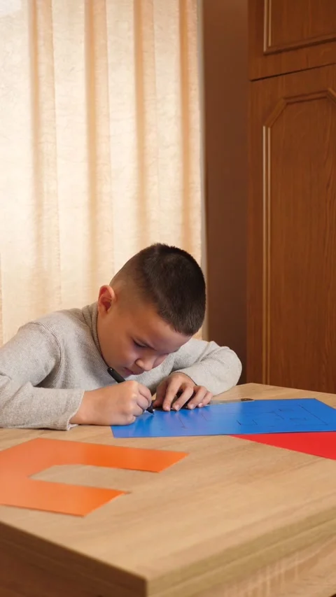 The boy makes a craft from colored cardboard, marking the contours. Stock Footage 314185161