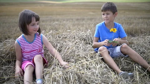 Boy makes a gift flower to a girl, sitting on hay, slow motion Stock Footage