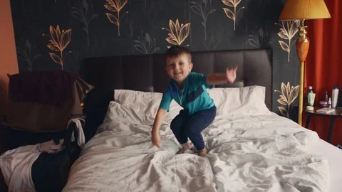 The boy makes high jumps on the double bed of his parents as if on a trampoline Stock Footage 124399983