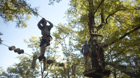 Boy makes his way across high wire in forest as family watches Stock Footage 103167732