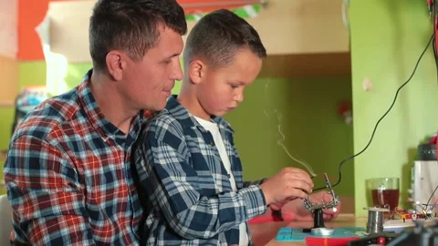 Boy makes hot joint using soldering iron looks magnifying glass, quality control Stockbeeldmateriaal 151749488