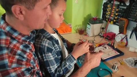 Boy makes hot joint using soldering iron looks magnifying glass, quality control Stockbeeldmateriaal 153842594
